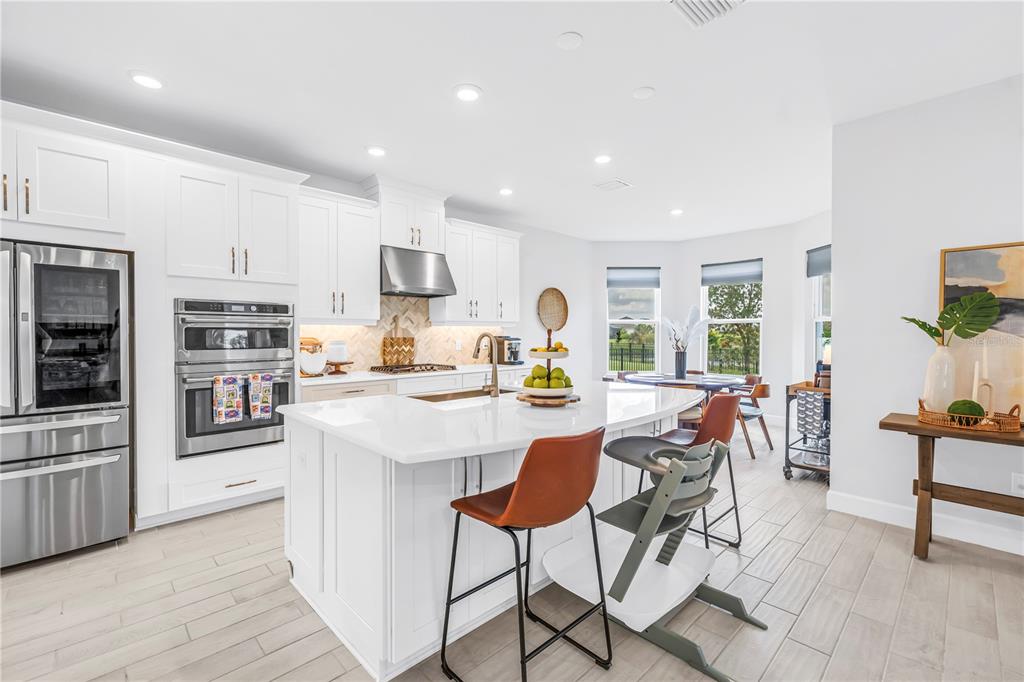 A modern kitchen features white cabinetry, a central island with bar seating, and tile flooring — 11133 FIELDSTONE DRIVE, PALMETTO, FL