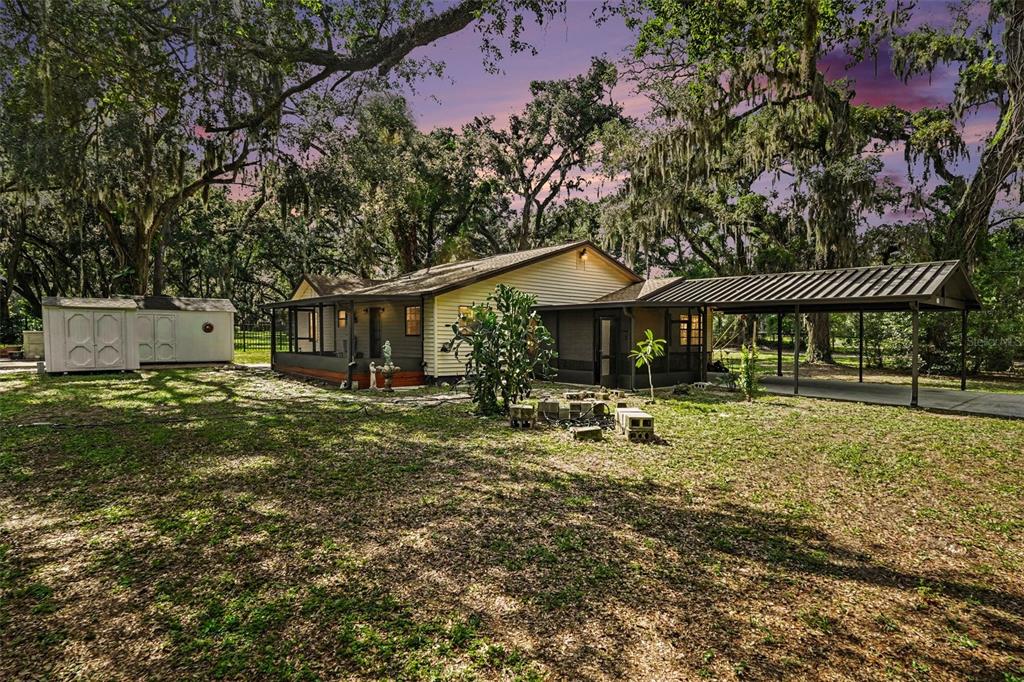 A single-story house with a metal carport and a detached shed under large oak trees — 231 DUKE SIMMS ROAD, BRANDON, FL