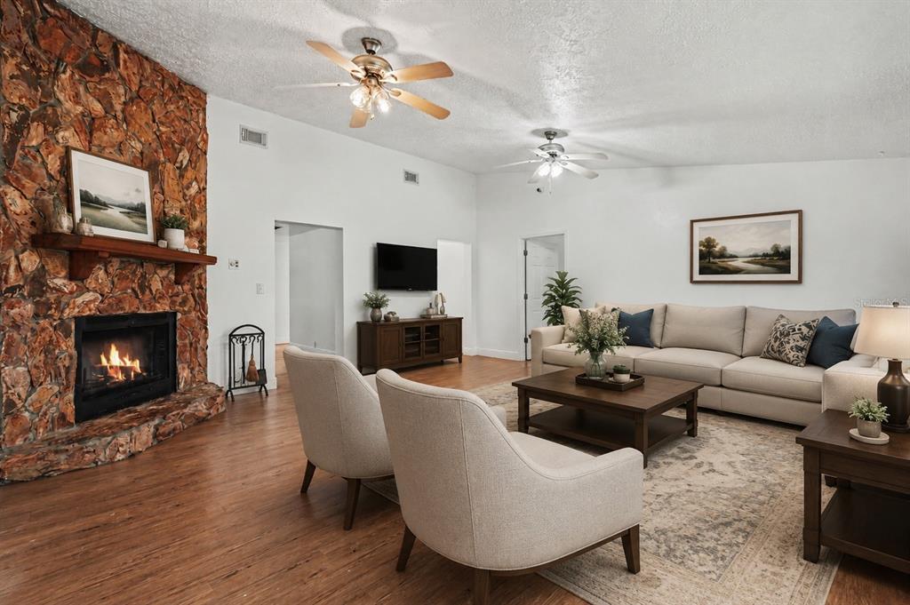 A living room features a stone fireplace, wood flooring, two ceiling fans, and neutral furniture — 231 DUKE SIMMS ROAD, BRANDON, FL