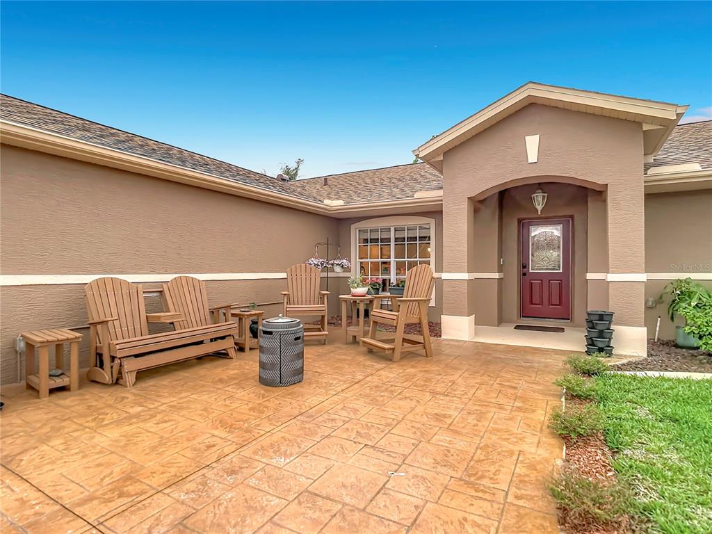 A tan house exterior features a stamped concrete patio with wooden chairs and a bench — 6353 CARDINAL CREST DRIVE, NEW PORT RICHEY, FL