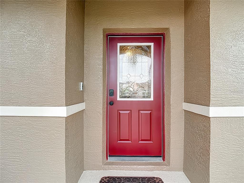 A red front door with a glass insert is set within a tan stucco entryway — 6353 CARDINAL CREST DRIVE, NEW PORT RICHEY, FL