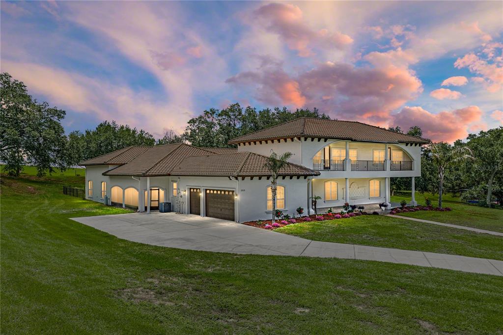 A two-story white house with a tiled roof and a concrete driveway at sunset — 37624 SKY RIDGE CIRCLE, DADE CITY, FL