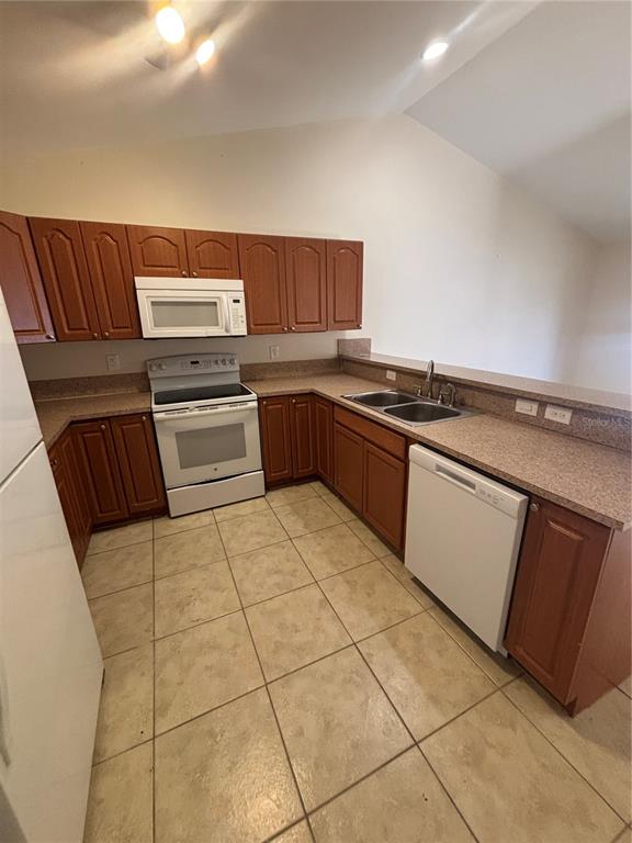 A kitchen features wood cabinets, white appliances, a double sink, and beige tile flooring — 2429 NOBEL AVENUE UNIT 2431, LEHIGH ACRES, FL