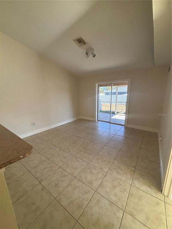 An empty room with beige tile flooring, a ceiling light, and a sliding glass door — 2429 NOBEL AVENUE UNIT 2431, LEHIGH ACRES, FL