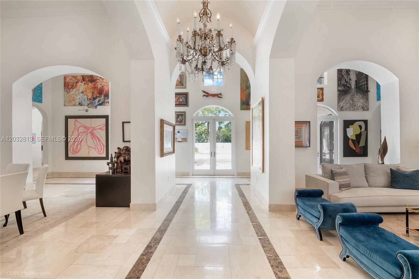 A bright, arched entryway features a crystal chandelier, marble floors, and numerous wall-mounted artworks — 7405 SW 104th St, Pinecrest FL 33156, PINECREST, FL