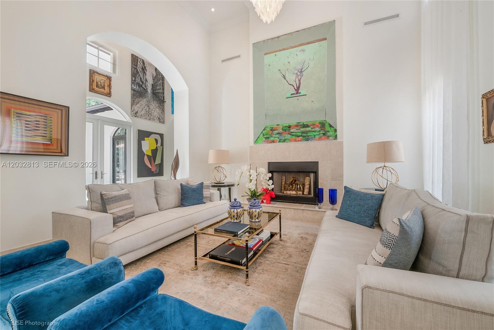 A living room features two beige sofas, blue armchairs, a fireplace, and large wall art — 7405 SW 104th St, Pinecrest FL 33156, PINECREST, FL