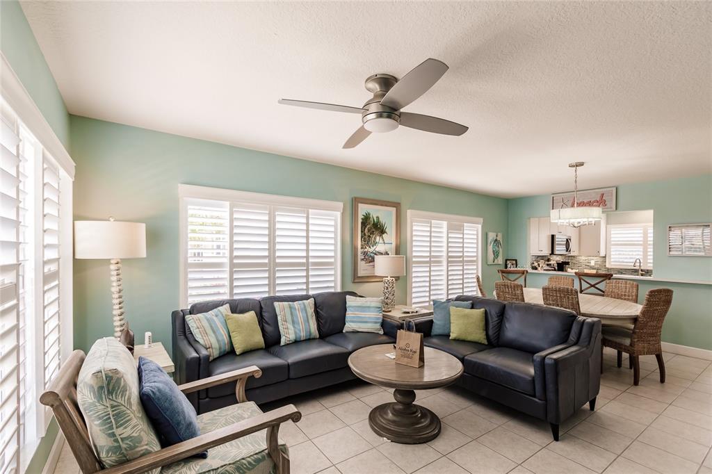 A living room and dining area featuring a dark leather sectional, tile floors, and shutters — 6020 MIDNIGHT PASS ROAD UNIT 2, SARASOTA, FL