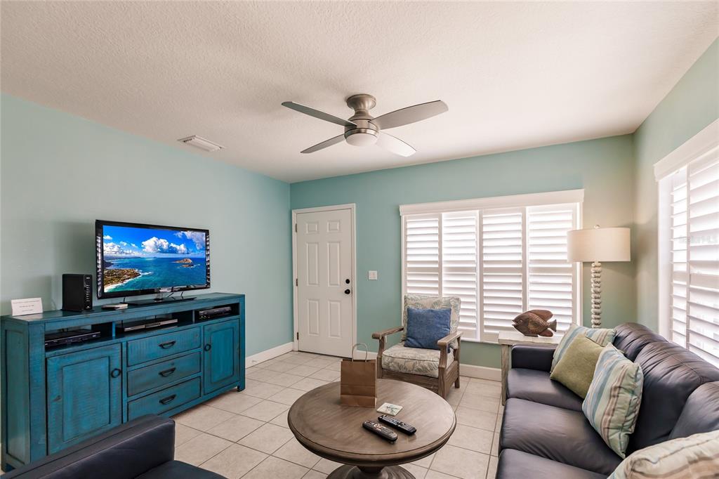 A living room features a blue media console, a dark sofa, and a ceiling fan — 6020 MIDNIGHT PASS ROAD UNIT 2, SARASOTA, FL