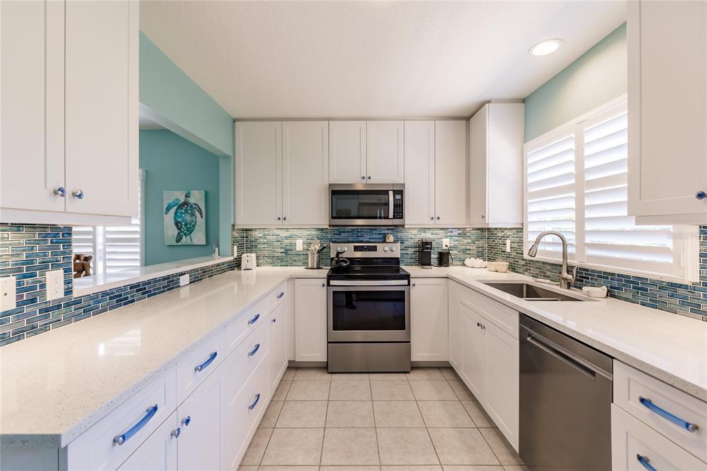 A kitchen features white cabinets, quartz countertops, stainless steel appliances, and a blue glass backsplash — 6020 MIDNIGHT PASS ROAD UNIT 2, SARASOTA, FL