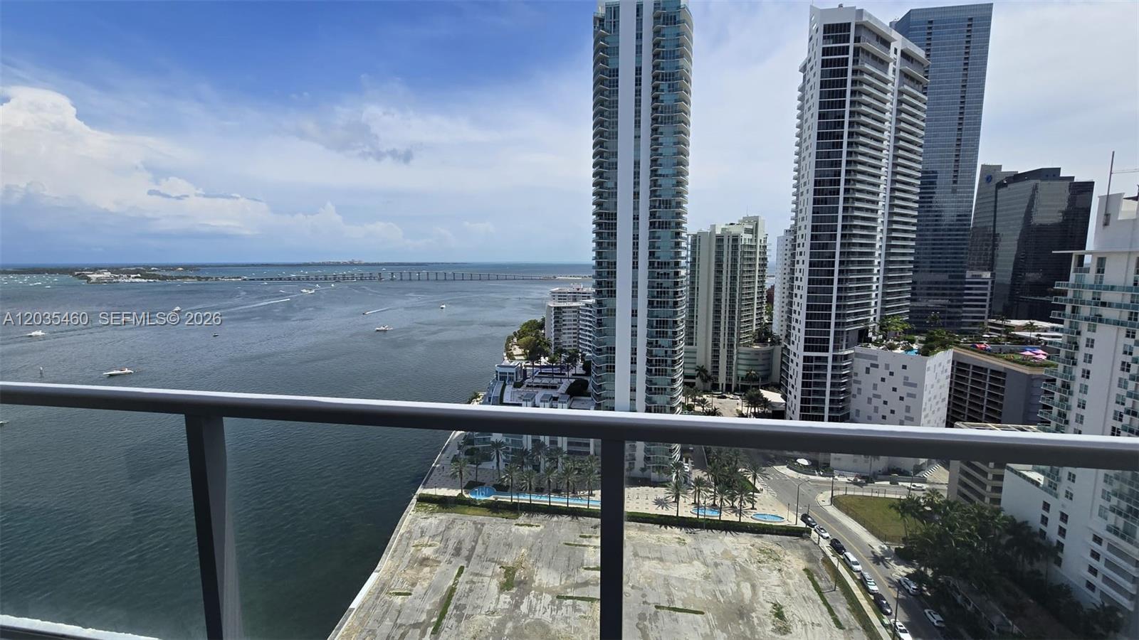 A high-rise balcony overlooks a bay, city skyscrapers, and a vacant waterfront lot — 1155 Brickell Bay Dr # 2507, Miami FL 33131, MIAMI, FL