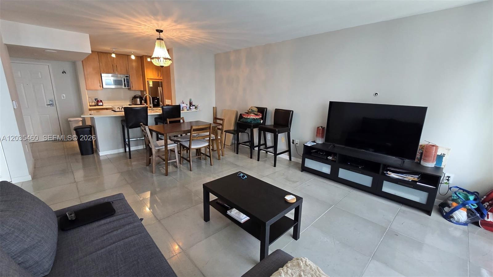 An open-concept living and dining area features tile flooring, a kitchen island, and a television — 1155 Brickell Bay Dr # 2507, Miami FL 33131, MIAMI, FL