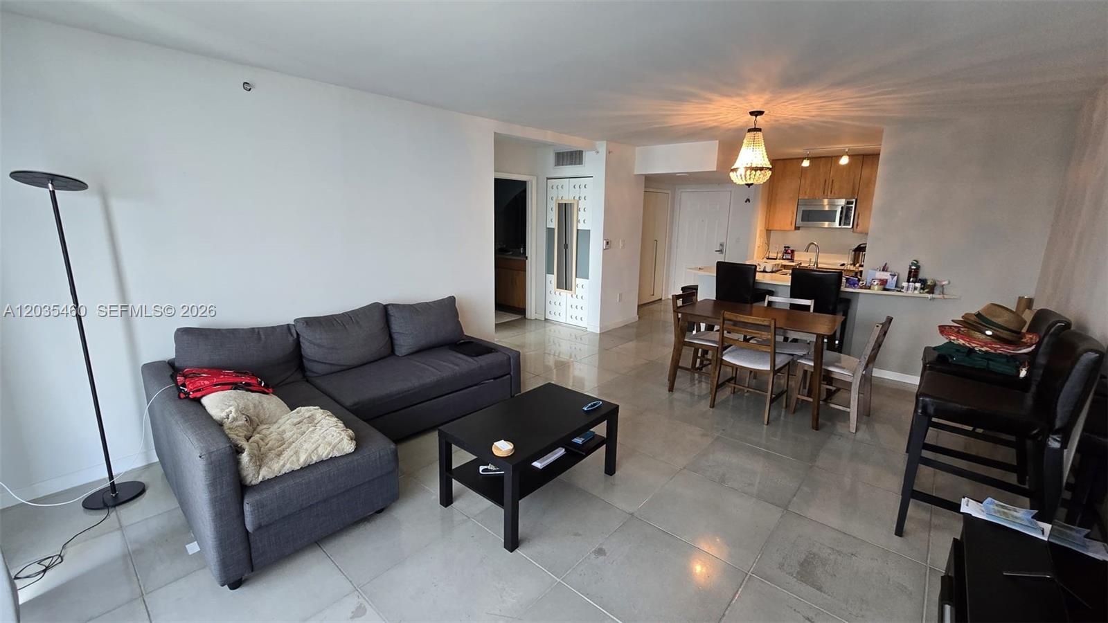 An open-concept living and dining area features tile flooring, a gray sectional, and a chandelier — 1155 Brickell Bay Dr # 2507, Miami FL 33131, MIAMI, FL