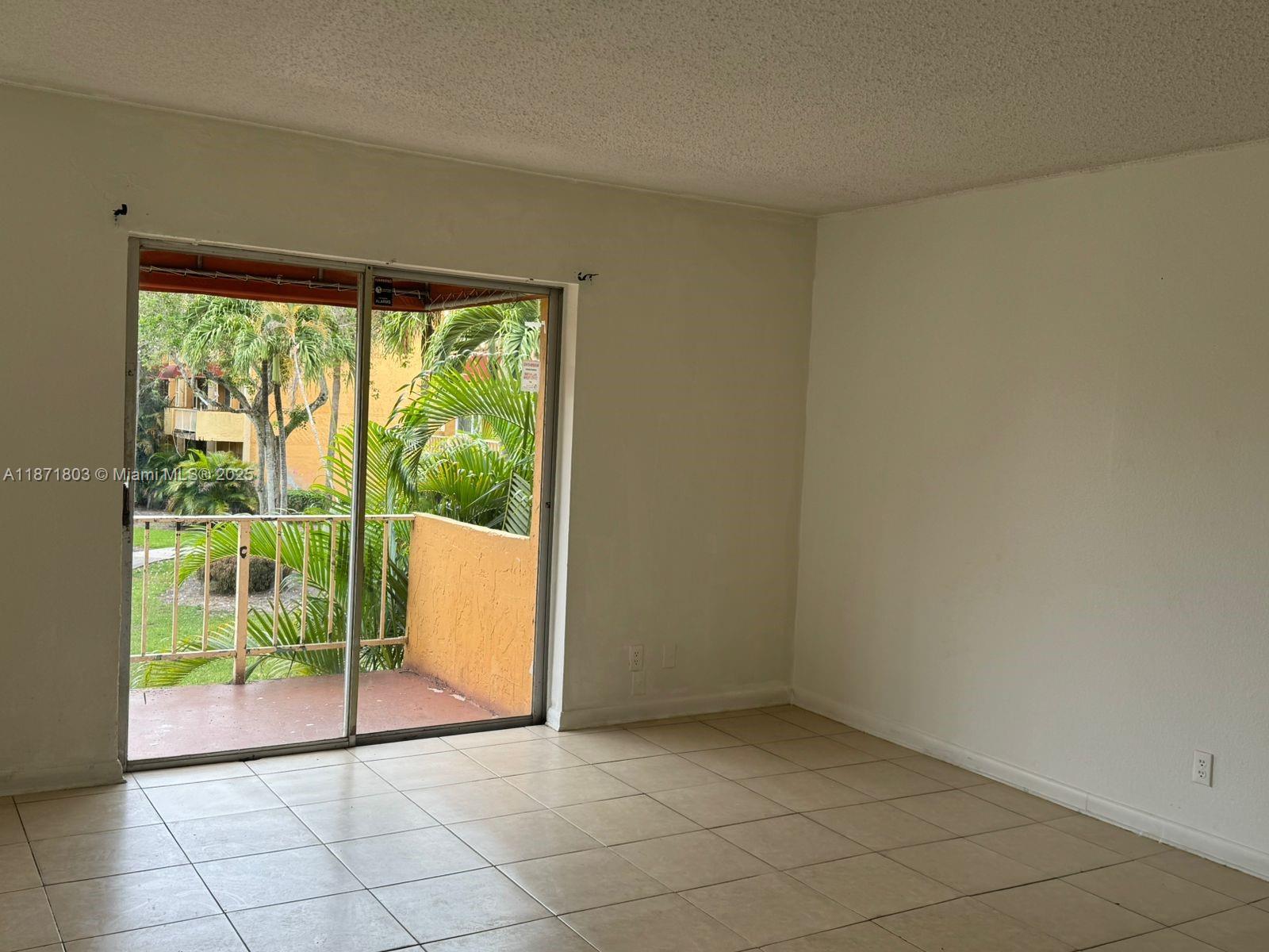 An empty room with beige tile flooring and a sliding glass door leading to a balcony — 17901 NW 68th Ave # T203, Hialeah FL 33015, HIALEAH, FL