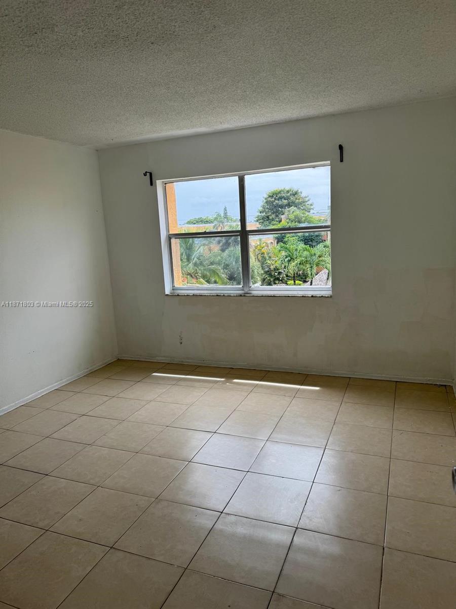 An empty room features beige tile flooring, white walls, and a window overlooking trees — 17901 NW 68th Ave # T203, Hialeah FL 33015, HIALEAH, FL