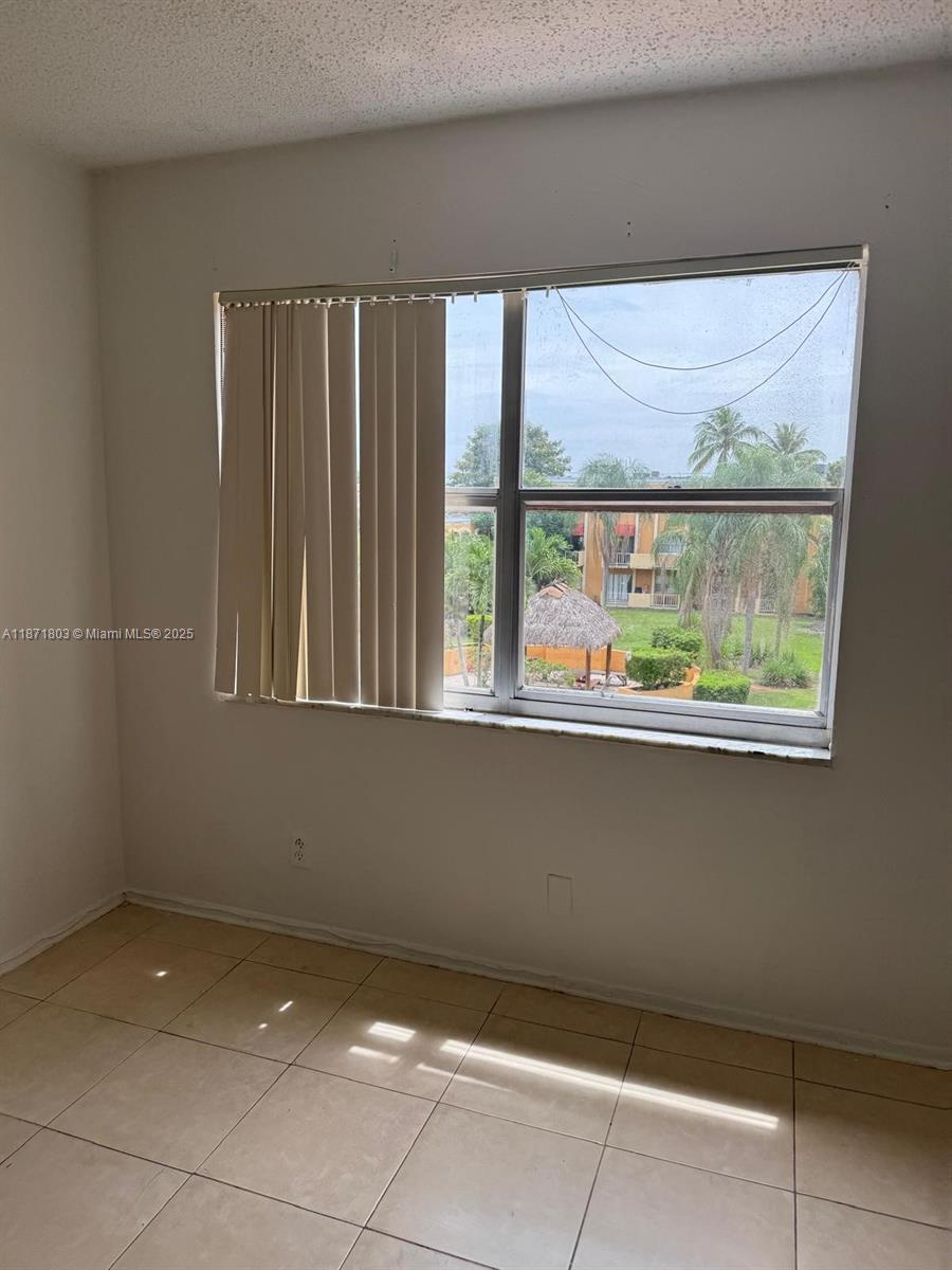 A room with beige tile flooring and a window overlooking a courtyard with palm trees — 17901 NW 68th Ave # T203, Hialeah FL 33015, HIALEAH, FL