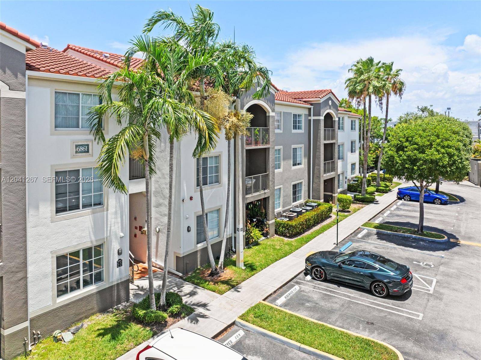 An exterior view of a multi-story apartment building with palm trees and a parking lot — 6861 SW 44th St # 202, Miami FL 33155, MIAMI, FL