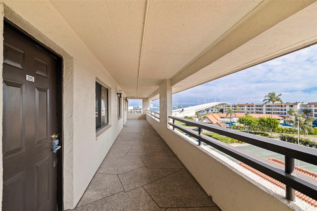 An outdoor apartment walkway features a dark door, stone flooring, and a view of a bridge — 106 1ST STREET E UNIT 315, TIERRA VERDE, FL