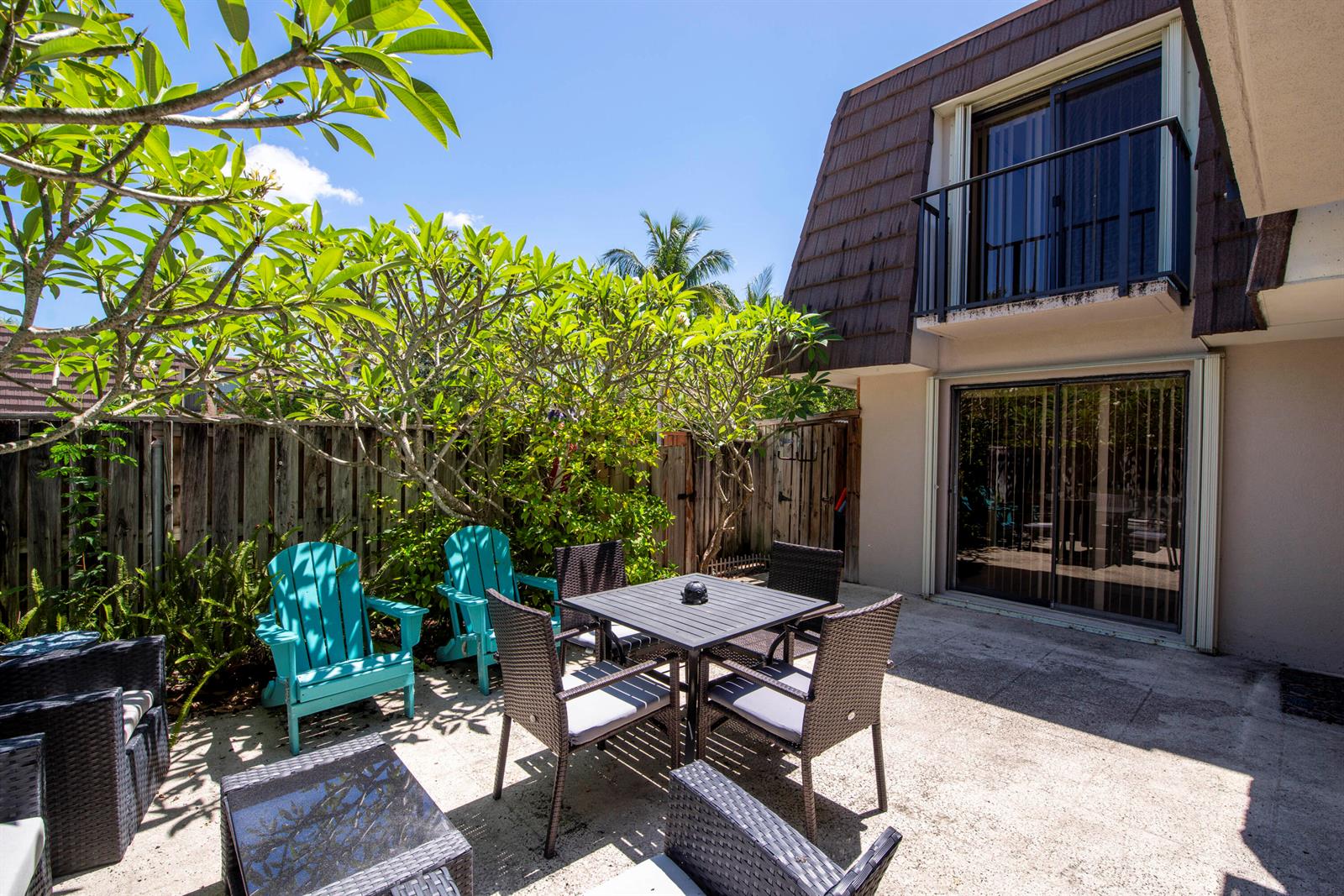 A patio with outdoor furniture sits beside a house with a balcony and sliding doors — 1913 19th Court, Jupiter FL 33477, JUPITER, FL