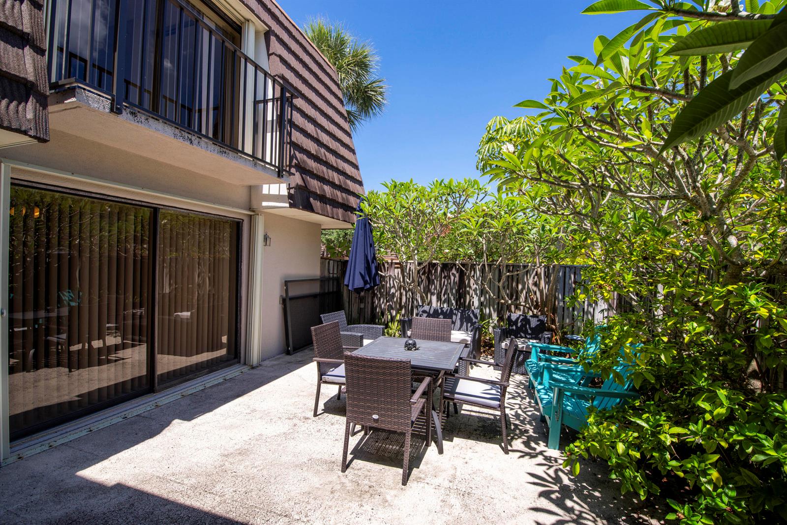 A patio features a dining set, blue chairs, and lush greenery next to a building exterior — 1913 19th Court, Jupiter FL 33477, JUPITER, FL
