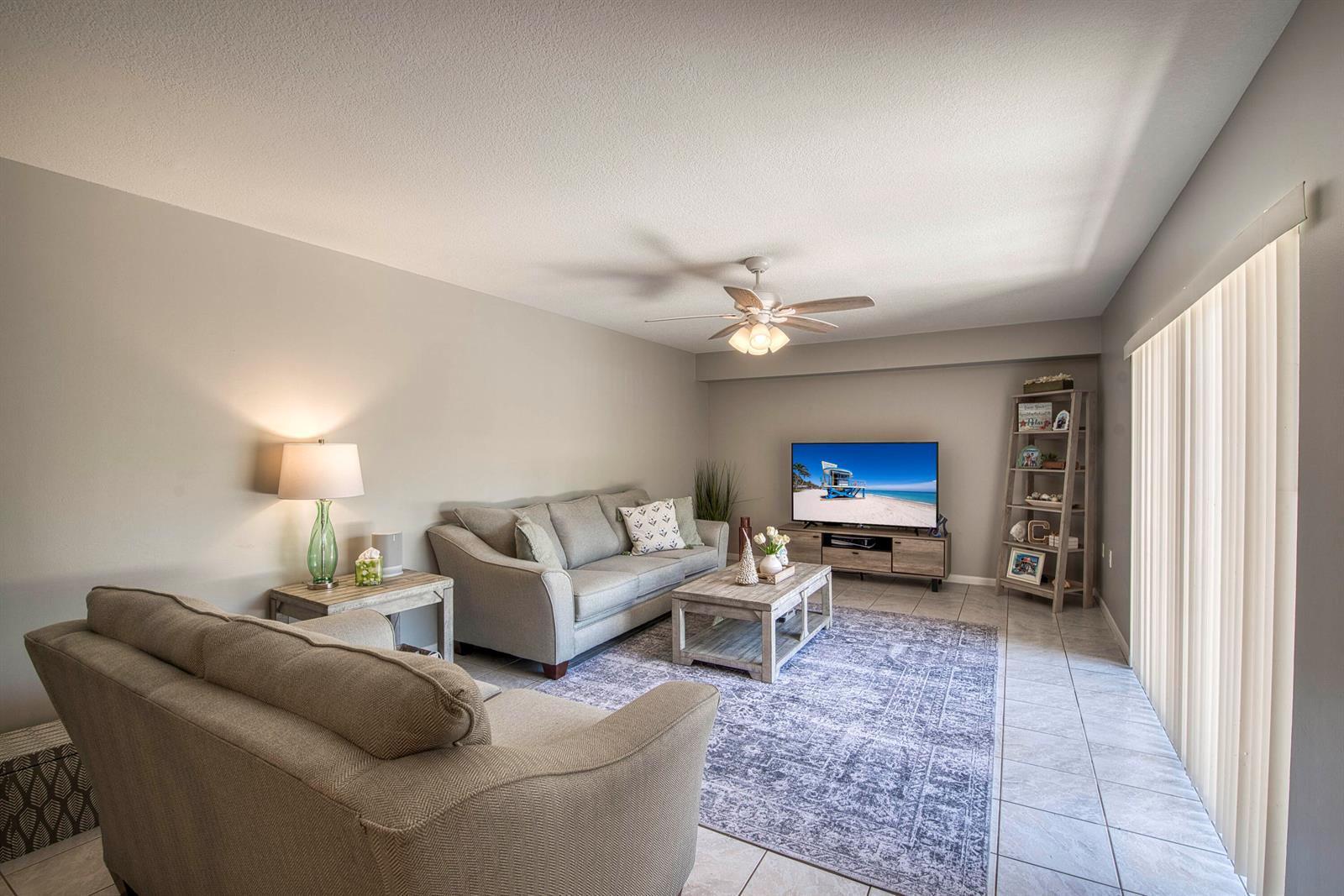 A living room features a gray sofa, a patterned area rug, and a television console — 1913 19th Court, Jupiter FL 33477, JUPITER, FL