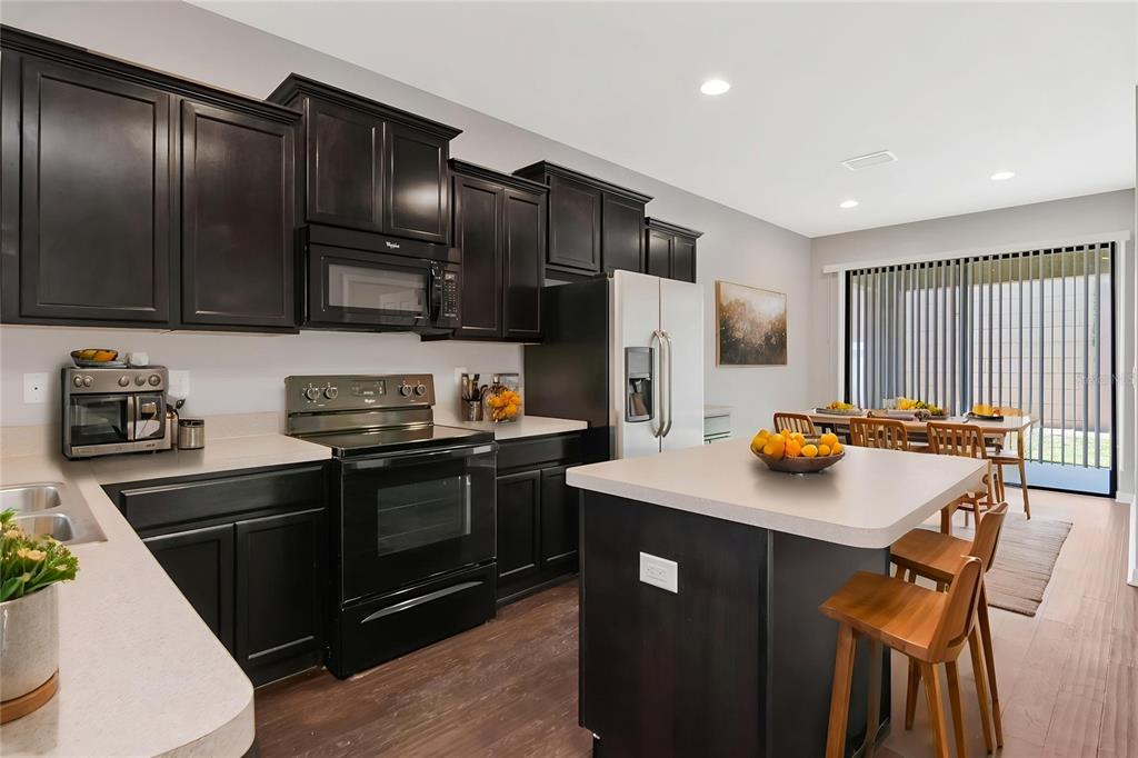 A kitchen features dark wood cabinets, black appliances, a central island, and a dining area — 6108 MAGNOLIA PARK BOULEVARD, RIVERVIEW, FL