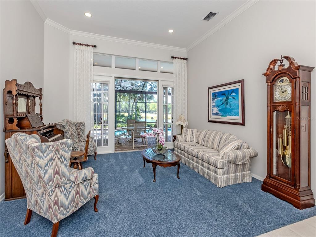 A living room features blue carpeting, a grandfather clock, patterned furniture, and sliding glass doors — 2120 MUSKOGEE TRAIL, NOKOMIS, FL
