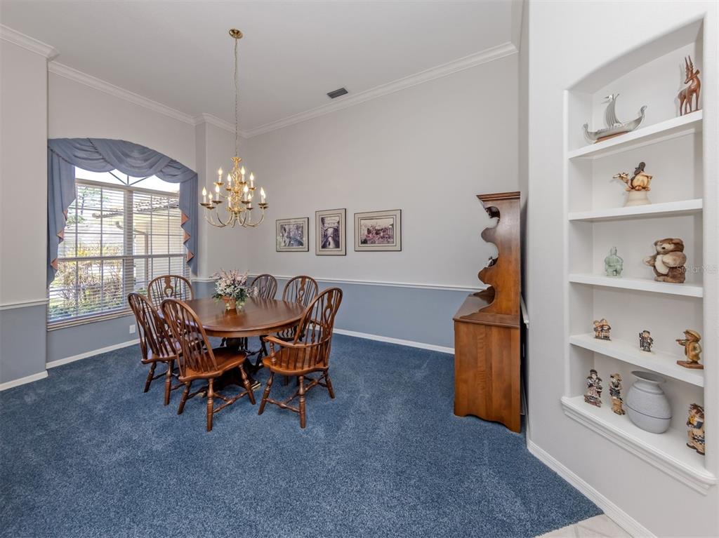 A dining room features blue carpeting, a wooden table with chairs, and built-in wall shelving — 2120 MUSKOGEE TRAIL, NOKOMIS, FL