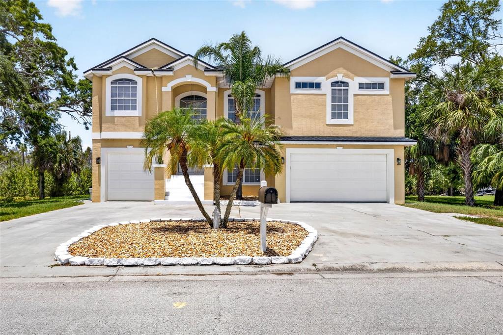 A two-story tan house with a three-car garage and a palm tree in the driveway — 7445 GULF WAY, HUDSON, FL