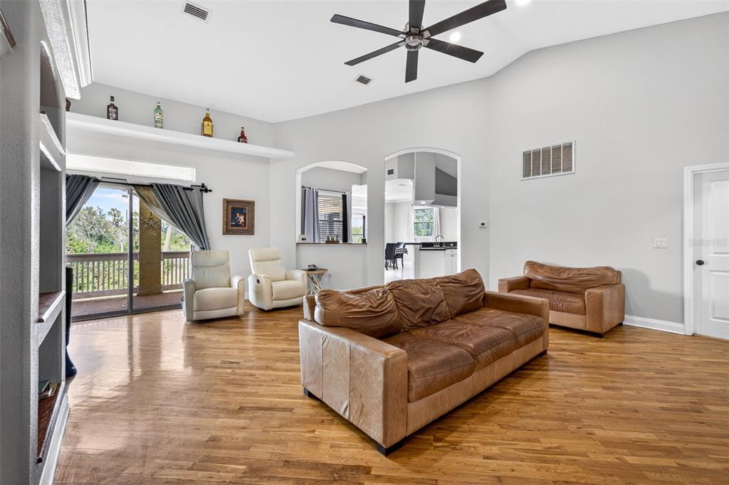 A living room features hardwood floors, a vaulted ceiling with a fan, and leather furniture — 7445 GULF WAY, HUDSON, FL