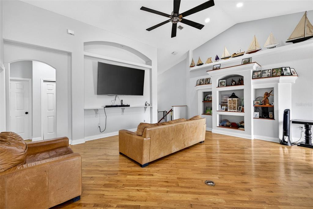 A living room features hardwood floors, a vaulted ceiling, a large television, and built-in shelving — 7445 GULF WAY, HUDSON, FL