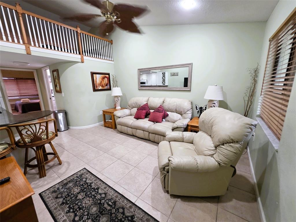A living room features a beige sofa, a matching recliner, tile floors, and a loft balcony — 20857 HAULOVER COVE UNIT B12, LUTZ, FL
