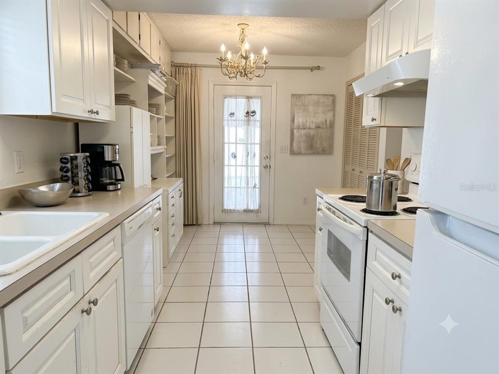 A white galley kitchen features tile flooring, white cabinetry, and a glass-paneled exterior door — 1561 AVALON BOULEVARD, CASSELBERRY, FL