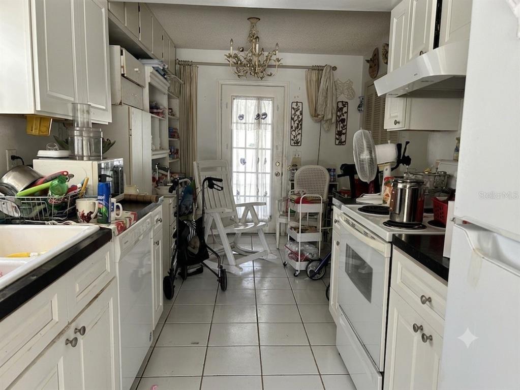 A galley-style kitchen features white cabinets, tile flooring, and a glass-paned door at the end — 1561 AVALON BOULEVARD, CASSELBERRY, FL