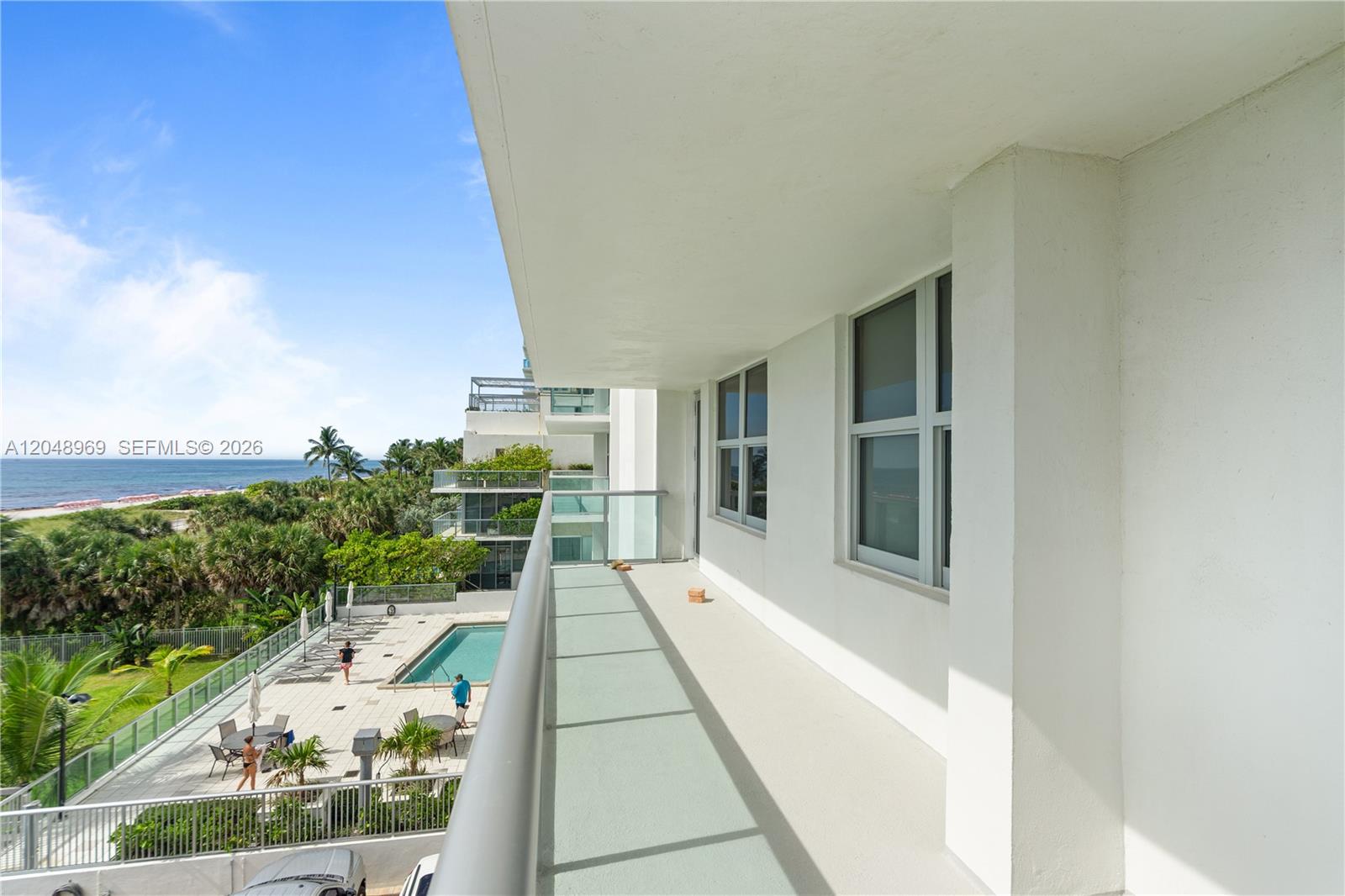 A balcony overlooks a swimming pool, lush greenery, and the ocean in the distance — 9511 Collins Ave # 403, Surfside FL 33154, SURFSIDE, FL