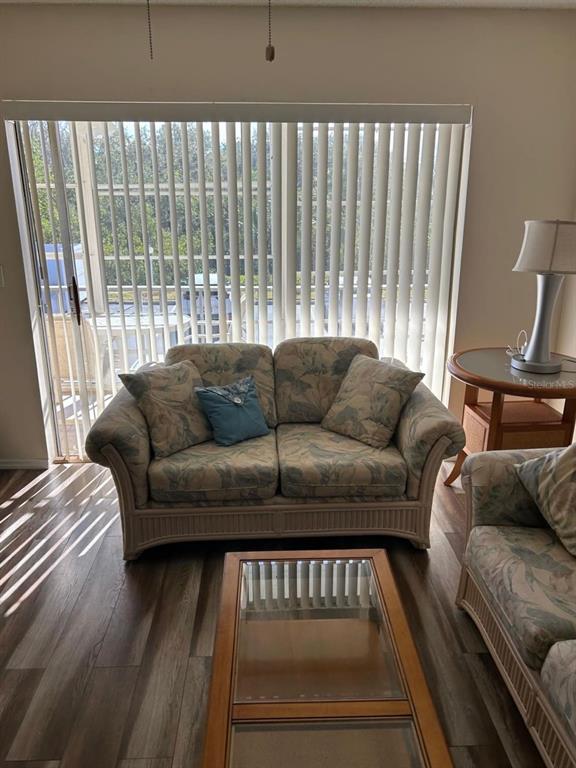 A living room features a floral loveseat, a glass-top coffee table, and vertical window blinds — 12760 INDIAN ROCKS ROAD UNIT 1048, LARGO, FL