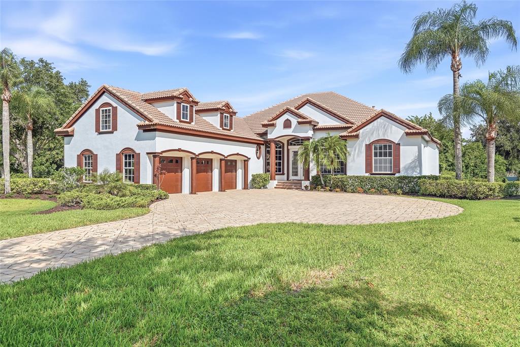 A white house with a three-car garage and a paved driveway sits on a lawn — 7618 PINE VALLEY STREET, BRADENTON, FL