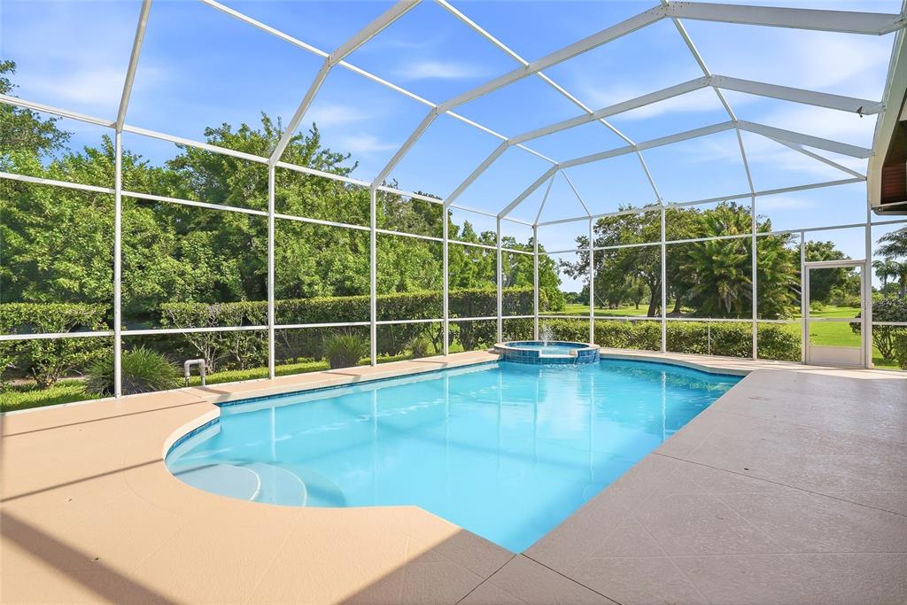 A screened-in swimming pool and spa area with a concrete deck and lush green landscaping — 7618 PINE VALLEY STREET, BRADENTON, FL