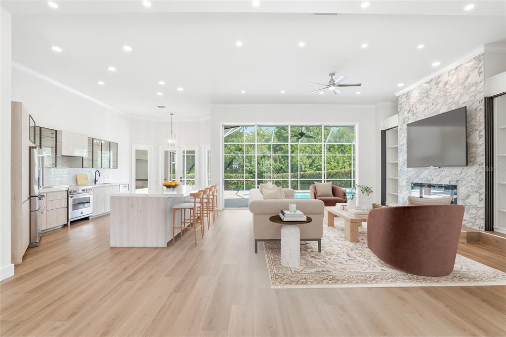 A bright open-concept living area features a modern kitchen, marble fireplace, and large glass doors — 7618 PINE VALLEY STREET, BRADENTON, FL