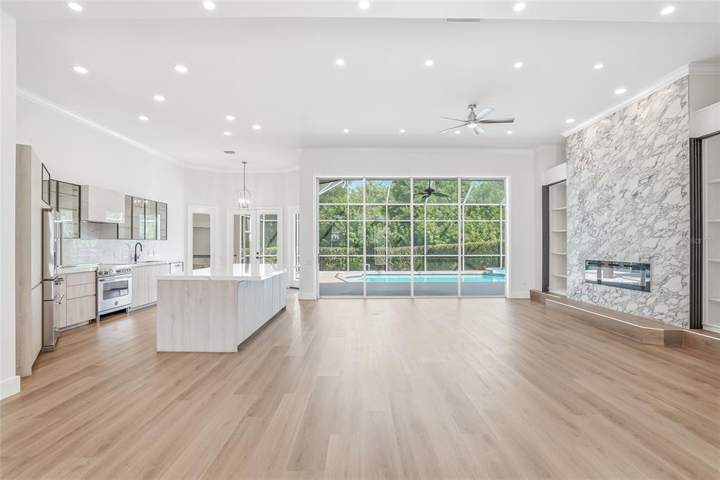 A modern open-concept kitchen and living area with light wood floors and a marble fireplace — 7618 PINE VALLEY STREET, BRADENTON, FL