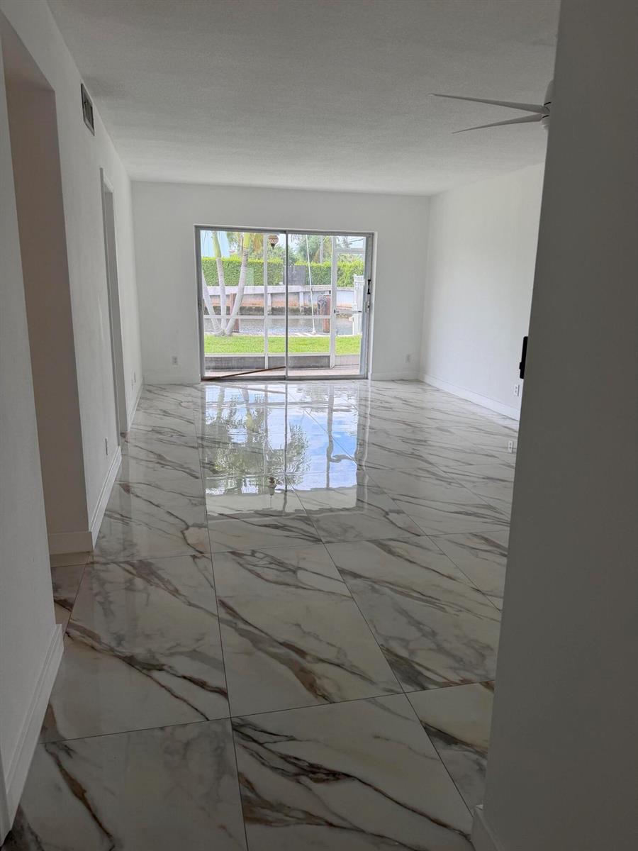 An empty room features large white marble-look floor tiles and a sliding glass door to a patio — 1100 Pine Drive # 102, Pompano Beach FL 33060, POMPANO BEACH, FL