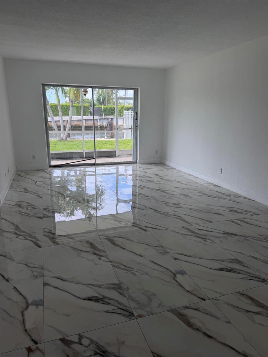 A bright, empty room features large white marble-patterned floor tiles and a sliding glass door — 1100 Pine Drive # 102, Pompano Beach FL 33060, POMPANO BEACH, FL