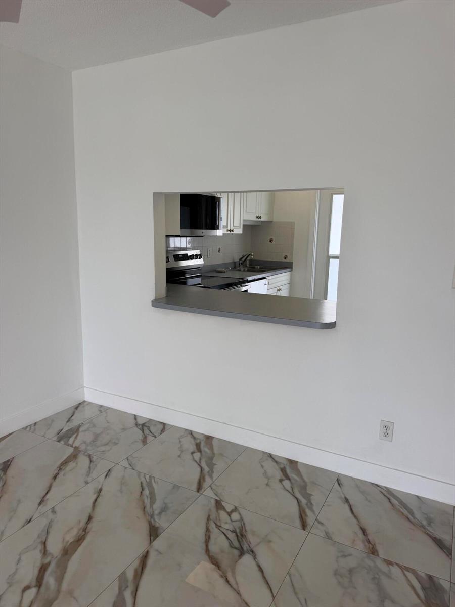 A view through a kitchen pass-through window into a kitchen with white cabinets and appliances — 1100 Pine Drive # 102, Pompano Beach FL 33060, POMPANO BEACH, FL
