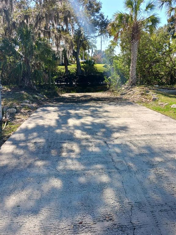 A concrete driveway leads toward a small canal surrounded by trees and lush vegetation — 5353 TROPICAL WOODS COURT, PORT RICHEY, FL