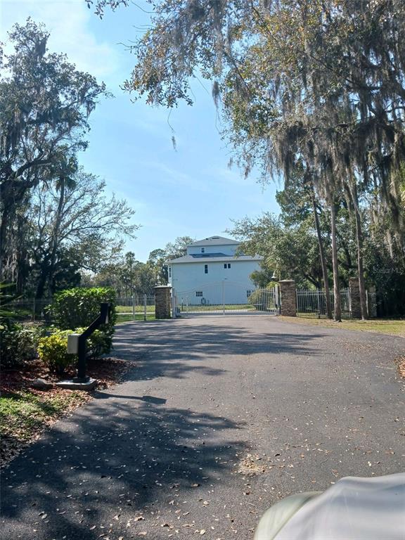A paved driveway leads to a gated entrance with a multi-story house in the background — 5353 TROPICAL WOODS COURT, PORT RICHEY, FL