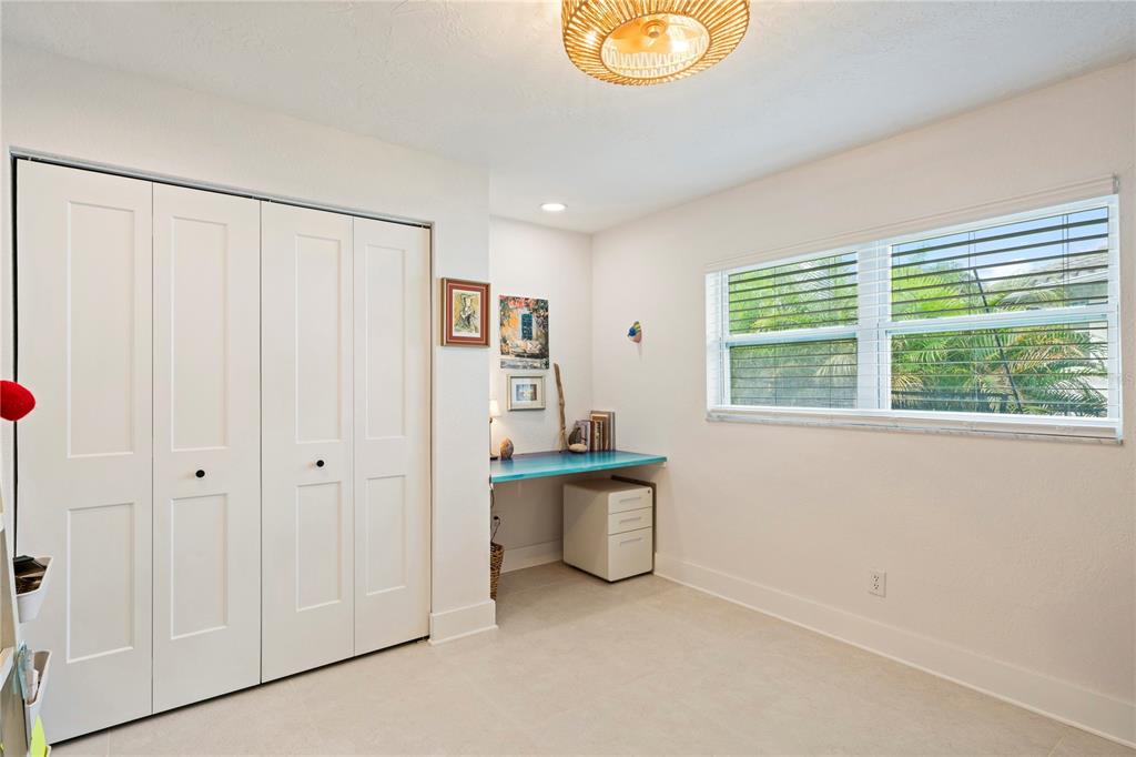 A bedroom with a built-in desk, white closet doors, tile flooring, and a large window — 1924 MICHIGAN AVENUE NE, ST PETERSBURG, FL