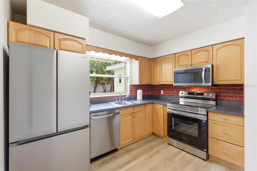 A kitchen with light wood cabinets, stainless steel appliances, and a red brick backsplash — 10651 125TH AVENUE, LARGO, FL