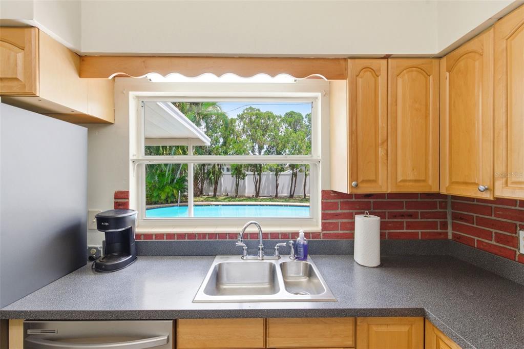 A kitchen sink area features light wood cabinets, a gray countertop, and a pool view — 10651 125TH AVENUE, LARGO, FL