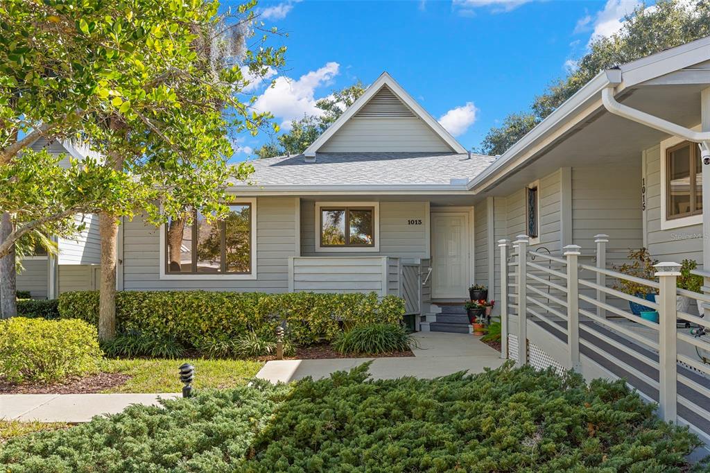 A light gray house exterior features a front entrance, a wooden ramp, and landscaped bushes — 1013 CARAVEL COURT, TARPON SPRINGS, FL