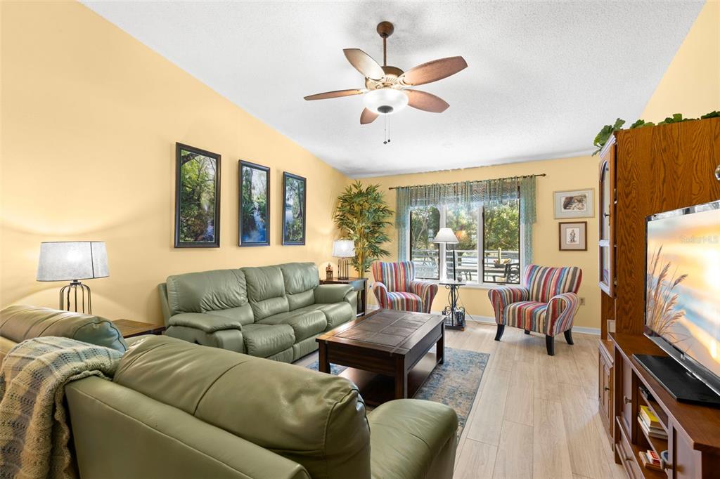 A living room features light yellow walls, green leather sofas, and a wooden coffee table — 1013 CARAVEL COURT, TARPON SPRINGS, FL