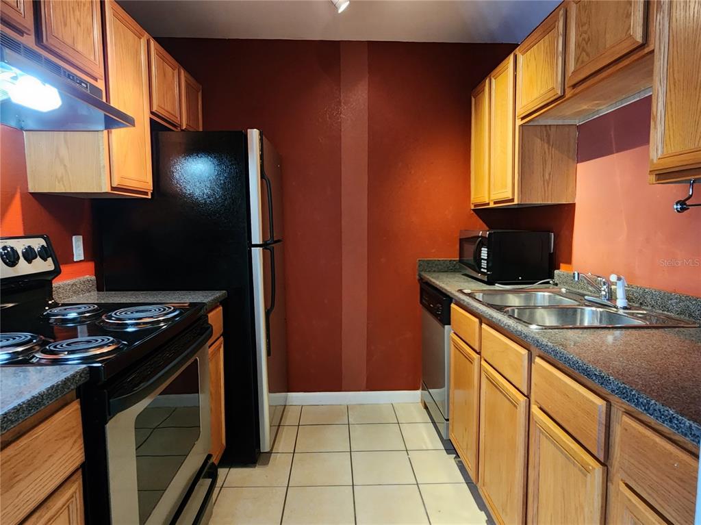 A kitchen features wood cabinets, dark countertops, a black refrigerator, and a stainless steel stove — 507 NW 39TH RD UNIT 237, GAINESVILLE, FL